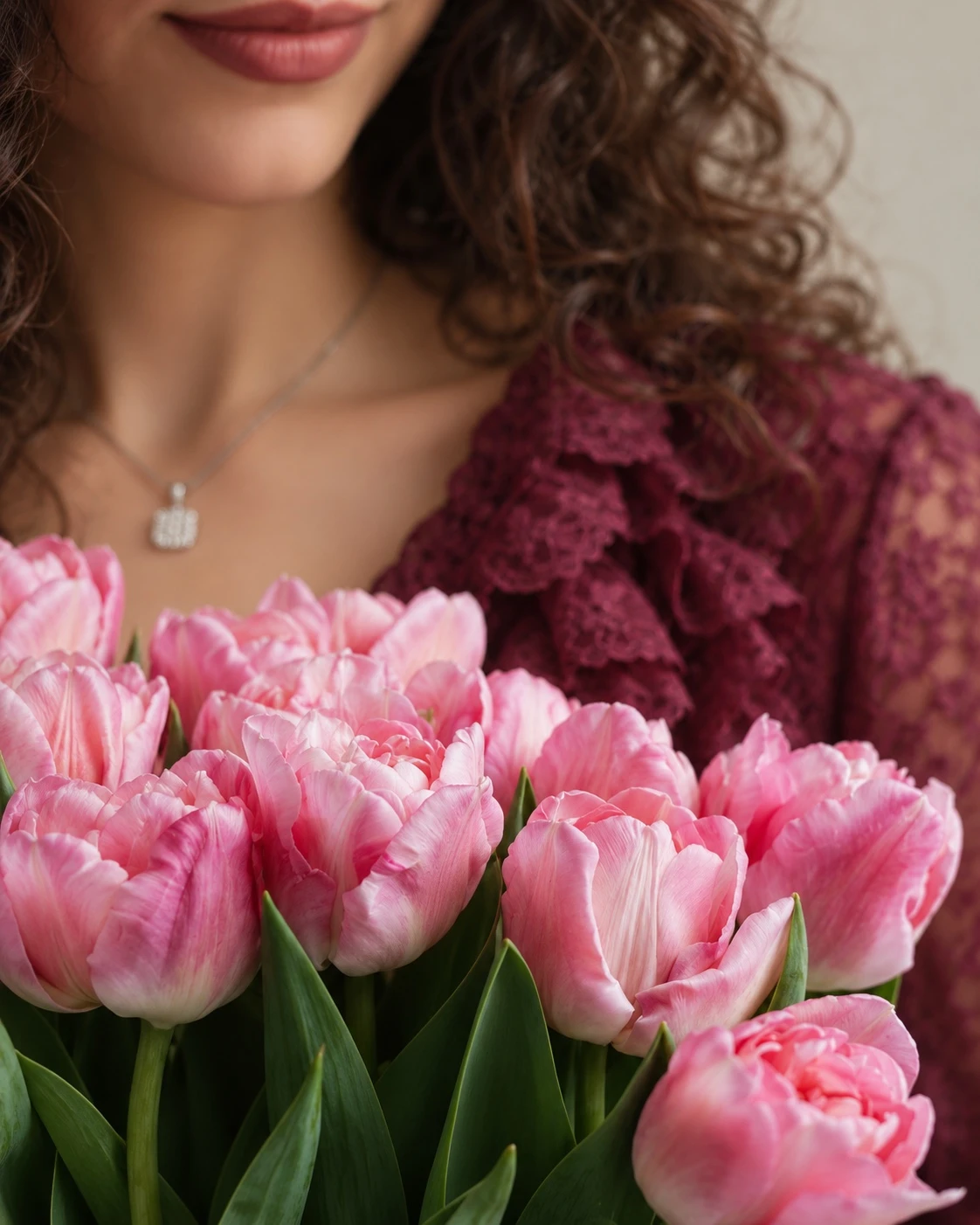 Dettaglio di una donna con una blusa cremisi e un bouquet di tulipani rosa